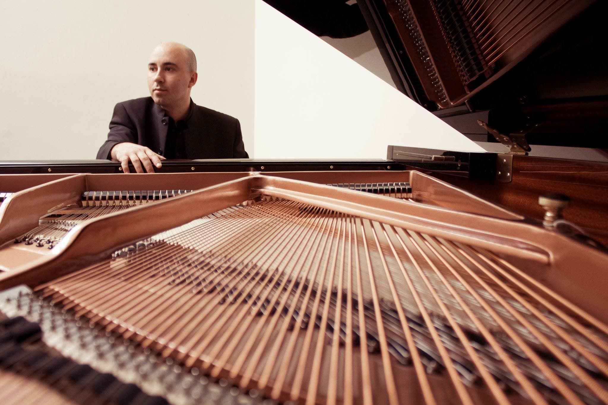 Artistic close-up of Juan Estay behind grand piano strings